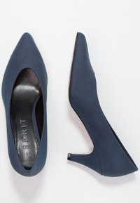 Escarpins bleu marine à bout pointu en matériau lisse, avec un talon bas et stable et un intérieur doublé de noir.