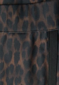 Leopardikuvioitu kangas ruskean ja mustan sävyissä, jossa on sileä pinta ja kontrastina mustat saumat reunaa pitkin.