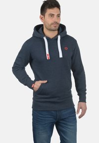 Sudadera con capucha azul marino hecha de un tejido de mezcla de algodón, con cordones blancos, un bolsillo tipo canguro y un pequeño logo en el pecho.