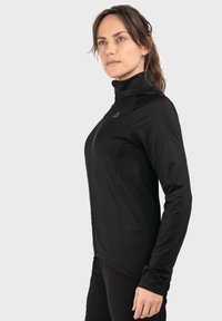 Schwarze Zip-Up-Jacke mit hohem Kragen, langen Ärmeln und tailliertem Schnitt. Der Stoff wirkt glatt mit leichtem Glanz und zeigt dezente Logodetails.