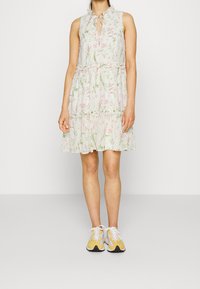 Abito floreale con scollatura arricciata, apertura a chiave e gonna a strati in tessuto leggero. Indossato con sneakers accentate di giallo.