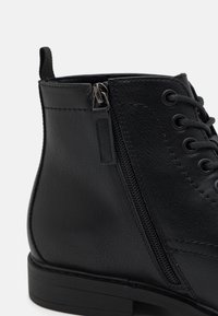 Botín negro de cuero hasta el tobillo con cremallera lateral y cordones redondos. Acabado texturizado, tacón bajo, costuras reforzadas y tira en la parte trasera.