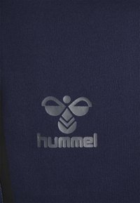Marineblauwe sportstof met een reflecterende zilveren "hummel" logo en bijen ontwerp aan de linkerkant. Glad van textuur met een aansluitende pasvorm.