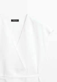 Robe blanche style portefeuille avec manches courtes et une fine ceinture à la taille, montrant une étiquette noire de la marque à l'intérieur de l'encolure.