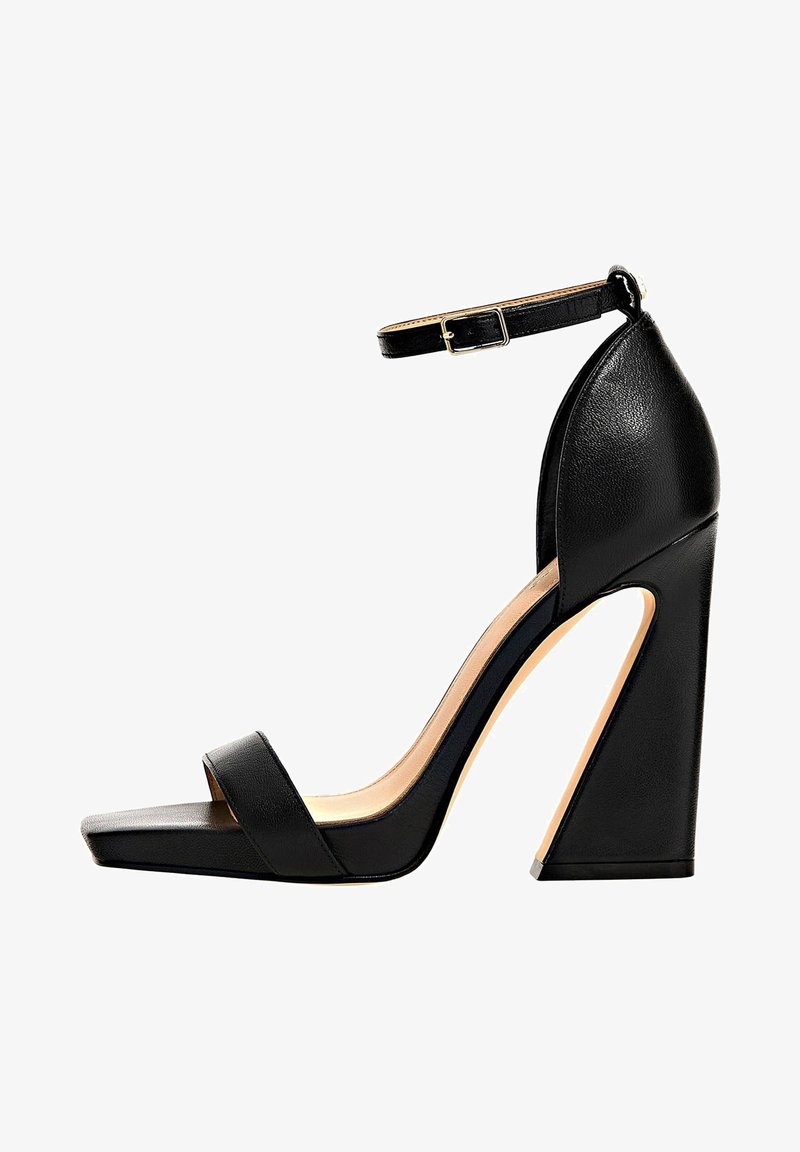 Sandale noire à talon haut avec un large talon carré, une sangle de cheville ajustable et une seule boucle pour les orteils. Matériau en cuir lisse, design à bout carré.