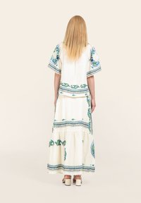 Maxikleid aus weißem Stoff mit blau-grünen Blumenmustern, kurzen Ärmeln und einem gestuften Rock mit dekorativem Saum.