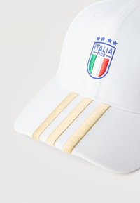 Λευκό καπέλο μπάιζμπολ με το έμβλημα της FIGC της Ιταλίας και τέσσερα αστέρια από πάνω, με τρεις χρυσές ρίγες στο καμπυλωτό γείσο.