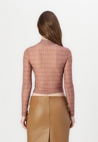 Halenka s dlouhým rukávem, přiléhavého střihu, vyrobená z průhledn�ého mauve materiálu se vzorem opakovaného loga. V kombinaci s hnědou koženou sukní s vysokým pasem.