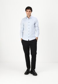 Világoskék gombos ing sötét gombokkal, karcsú fazonban, hosszú ujjú, fekete nadrággal és fekete cipővel párosítva. Minimalista design, sima textúra.