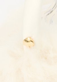 Lumânare albă cu suport metalic auriu în formă de inimă, înconjurată de pene decorative albe și pufoase.