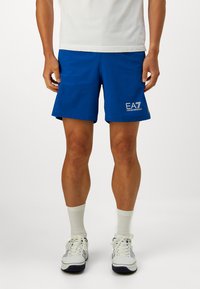 Kék sportnadrág könnyű anyagból, sima felülettel és rugalmas derékrésszel, fehér "EA7 Emporio Armani" logóval.