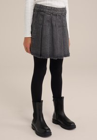 Szürke farmer szoknya redőkkel és rojtos szegéllyel, fekete leggings-szel és bokacsizmával párosítva. A szoknya derékrészén varrási részletek találhatók.