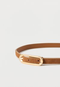 Ceinture fine en suède marron clair avec boucle ovale brillante en or sur fond blanc.