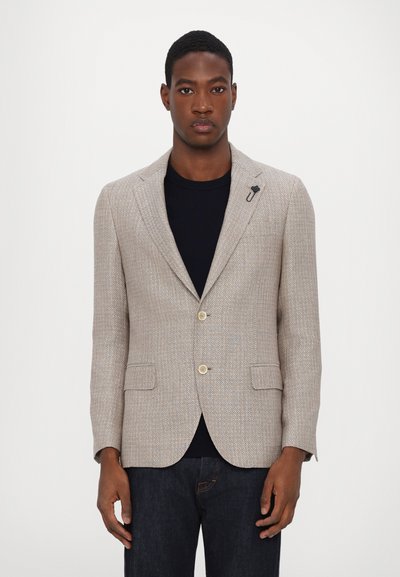 Beige textured blazer with notched lapels, two front buttons, and side pockets, worn over a black shirt, paired with dark jeans.
