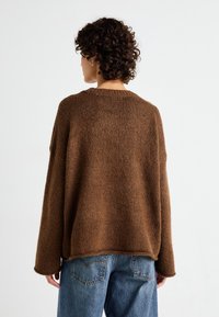 Pull en tricot brun en laine douce et texturée, avec une coupe décontractée et des épaules tombantes. Assorti à un jean taille haute.