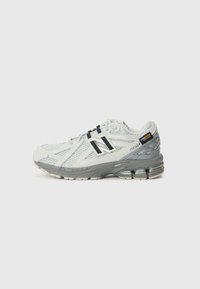 Adidași de alergare gri deschis, cu o parte superioară din plasă, accente negre și o talpă texturată. Modelul este New Balance 1906R, cu detalii de amortizare.