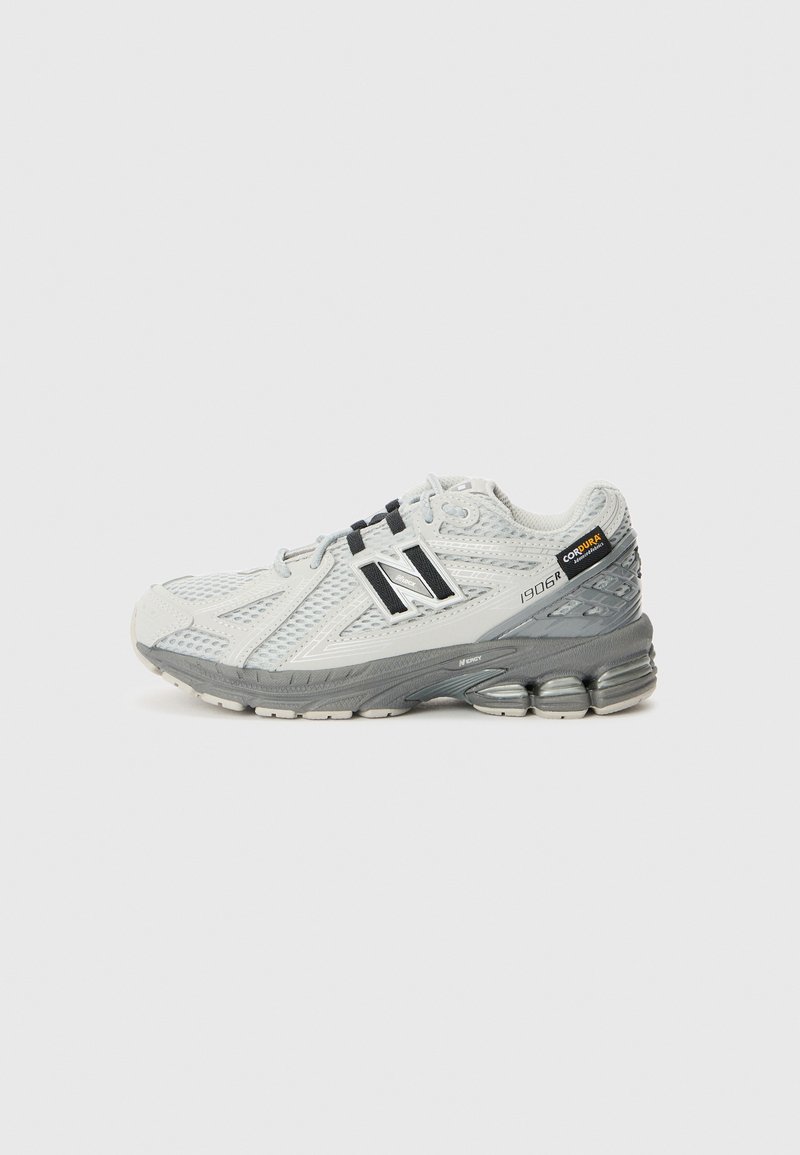 Adidași de alergare gri deschis, cu o parte superioară din plasă, accente negre și o talpă texturată. Modelul este New Balance 1906R, cu detalii de amortizare.