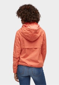 Lättvikts orange jacka med huva och design med bakstycke, elastiska ärmslut och en avslappnad passform. Kombinerad med denimjeans.