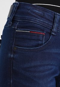 Tummansiniset farkut, joissa on punavalkoinen tikkaus pienessä kolikkotaskussa, yhdistetty mustaan paita, joka on laitettu housuihin.