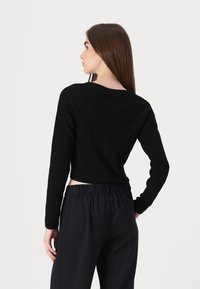 Μαύρη ριμπ μπλούζα με μακριά μανίκια και cropped γραμμή, διαθέτει στρογγυλή λαιμόκοψη και ράγκλαν μανίκια, συνδυασμένη με σκούρους, φαρδείς παν trousers.