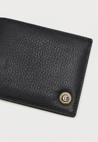 Mustat nahkainen lompakko, jossa on näyttävä kultasävyinen pyöreä metallikilpi ja ommellut reunat.