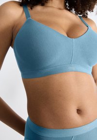 Ljusblå bralette i mjukt tyg med justerbara axelband, med en sömlös design och en logoband i nederkant.