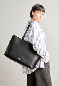 Schwarze Leder-Shopper-Tasche mit strukturierter Form, ausgestattet mit glatter Textur, goldenen Hardware-Details und einem dezenten Logo am Boden.