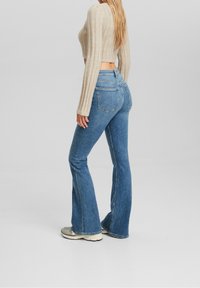 Blue denim flared jeans with a high waist, featuring rear pockets and a smooth texture, paired with a light-colored ribbed crop top.