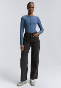 Bluza albastru deschis cu mâneci lungi și model cu dungi, cu detalii de nasturi, asortată cu blugi negri largi, cu talie înaltă, și adidași albastru deschis.