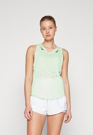 Lichtgroen mouwloos sporttopje met perforaties, ronde halslijn en een zwart logo. Gecombineerd met witte shorts, met een gladde stofstructuur.