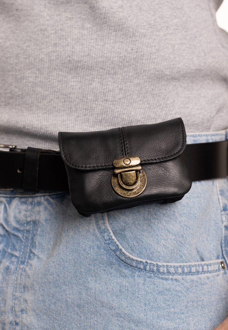 Black leather pouch with curved flap closure and brass hardware, attached to a dark belt, worn over light denim jeans.