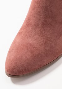 Różowe zamszowe botki za kostkę z ostrym noskiem i gładką fakturą. Podeszwa jest płaska, o minimalistycznym wzornictwie i subtelnych detalach w szwach.