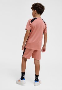 Ensemble de sport rose clair composé d'un haut à manches courtes avec des accents noirs et un short assorti. Porté avec des chaussettes noires et des baskets blanches.