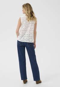 White, sleeveless top with floral lace pattern, paired with loose blue denim jeans and brown block-heeled shoes.