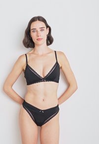 Ensemble de lingerie noir comprenant un soutien-gorge triangle et une culotte taille haute. Détails en dentelle et un petit nœud sur la culotte.
