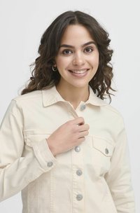 Veste en denim de couleur crème avec un col, devant boutonné et deux poches poitrine. Équipée de boutons en métal argenté et d'une coupe décontractée.
