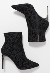 Bottines noires à talons hauts avec bouts pointus, fermetures éclair latérales et motif léopard subtil sur la surface en tissu.