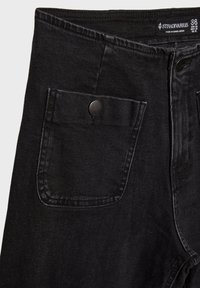 Schwarze Denim-Jeans mit klassischem Design, vorderer Tasche, metallischem Knopfverschluss und robusten Nähten. Größenschild sichtbar: 38.
