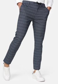 Granatowe spodnie w kratę wykonane z lekkiego materiału, z gumką ze sznurkiem w pasie i bocznymi kieszeniami, zestawione z białymi trampkami.
