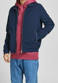 Námořnická bunda na zip přes růžovou mikinu s kapucí, s žebrovanými manžetami a lemem, v kombinaci s modrými džíny. Hladká tkanina, minimální kovové detaily.