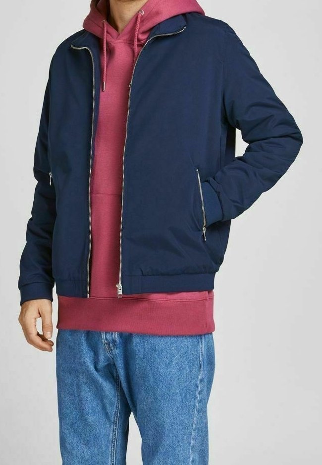 Námořnická bunda na zip přes růžovou mikinu s kapucí, s žebrovanými manžetami a lemem, v kombinaci s modrými džíny. Hladká tkanina, minimální kovové detaily.