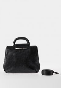 Musta nahkainen käsilaukku, jossa on rakenne, pyöreät yläkahvat ja irrotettava hihna. Etuosassa on metallinen yksityiskohta.