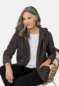 Veste zippée à capuche en polaire gris foncé au toucher texturé, dotée d'une poche avant et d'une capuche avec cordon de serrage, portée sur une chemise blanche.