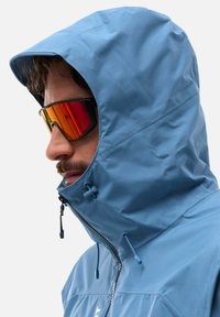 Blaue wasserdichte Jacke mit Kapuze und hohem Kragen, verstellbaren Kordeln und Reißverschluss. Enthält reflektierende Sonnenbrille mit einem Verlaufsglas.