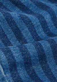 Denimstoff in verschiedenen Blautönen mit einem subtilen Wellenmuster. Die Textur erscheint weich und leicht abgenutzt, wobei feine Webdetails zur Geltung kommen.