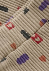 Beige geripptes Gewebe mit roten, lila, schwarzen und braunen verspielten Herzen und abstrakten Formen, die im Nahaufnahme sichtbar sind.