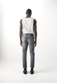 Fitted grå denimjeans med en subtil tvätt och två bakfickor, i kombination med en ärmlös vit bomullstopp och svarta skor.