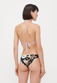 Lila nyakpántos bikini, fekete alsó résszel, amely virágmintákkal van díszítve, sárga és narancssárga virágokkal, minimális takarást biztosít.