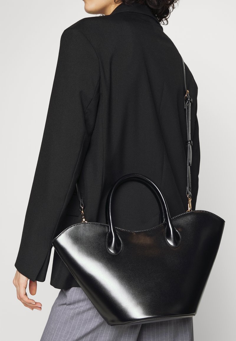 Sort læderveske med et struktureret, vinklet design, glat tekstur, dobbelte håndtag og en aftagelig rem, accentueret med guldfarvet hardware.