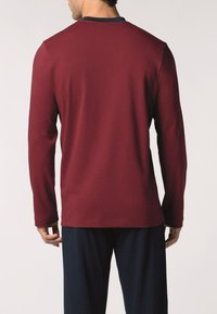 La camicia a maniche lunghe in tessuto bordeaux presenta un collo a girocollo con un accento blu navy. Il retro mostra una texture liscia e una vestibilità rilassata.